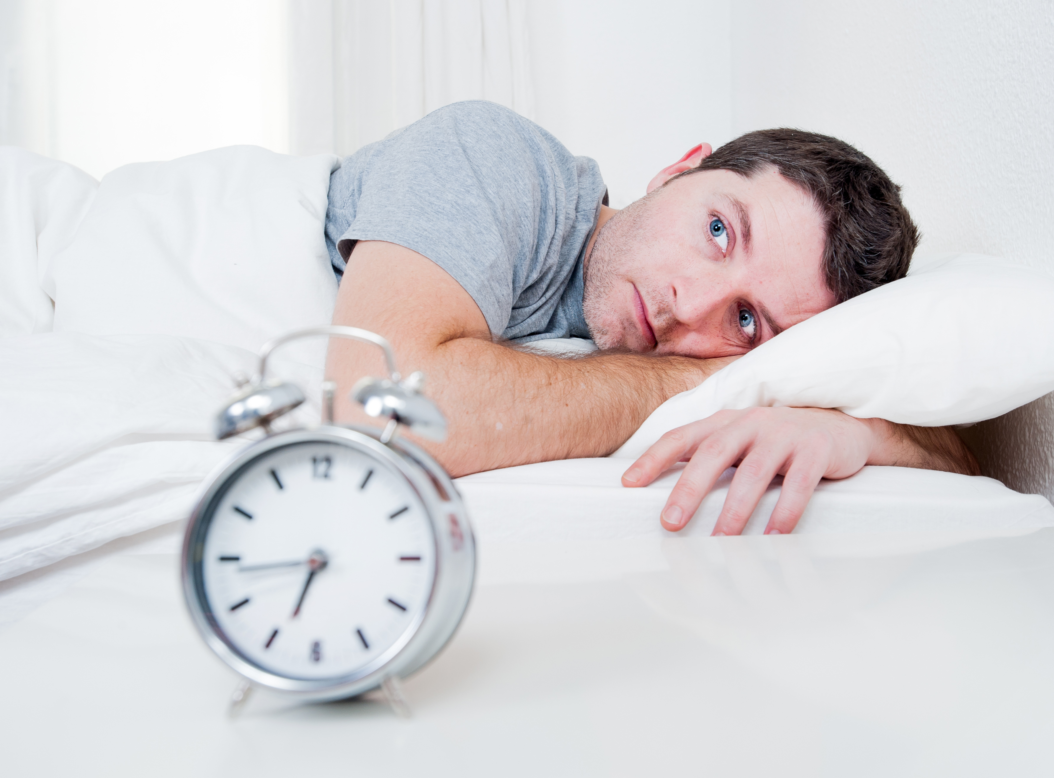 Homem com olhar atento deitado na cama como sintoma da paralisia do sono