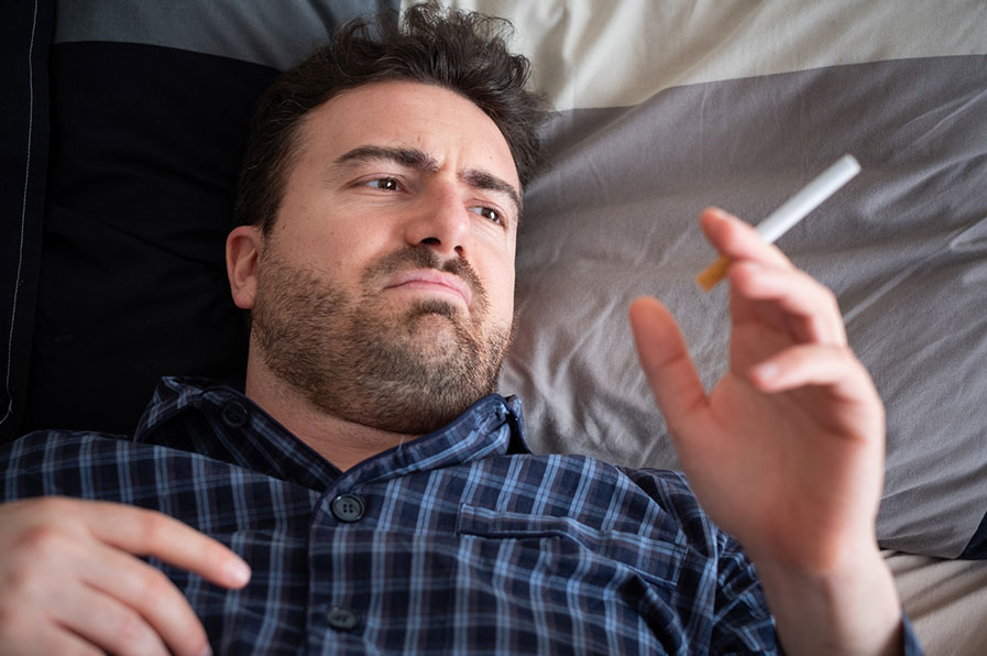 Homem deitado, fumando na cama