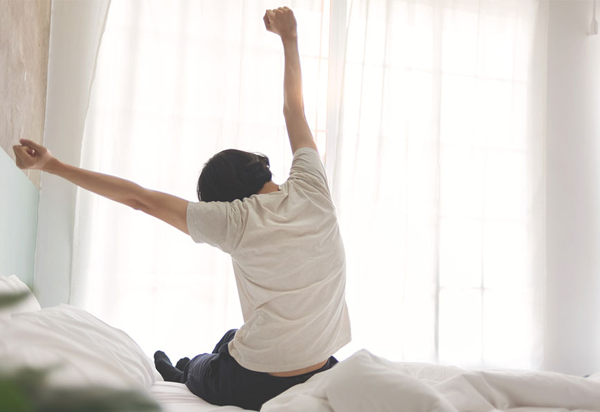 Homem sentado na cama se espreguiçando